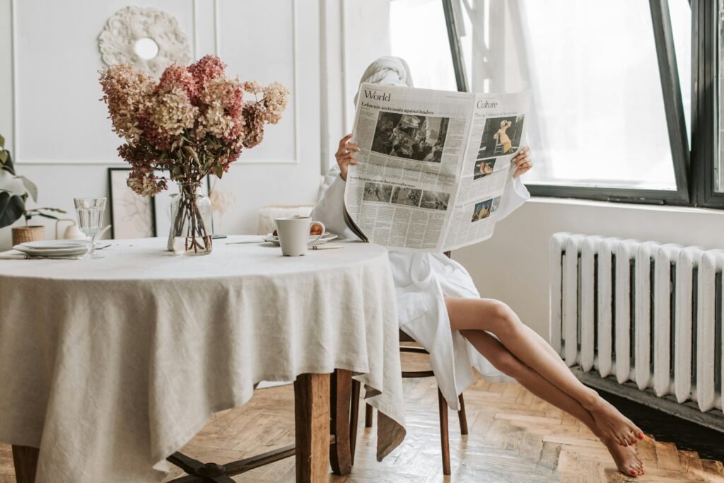 Woman enjoying a relaxing morning, reading a newspaper with coffee in a cozy setting.